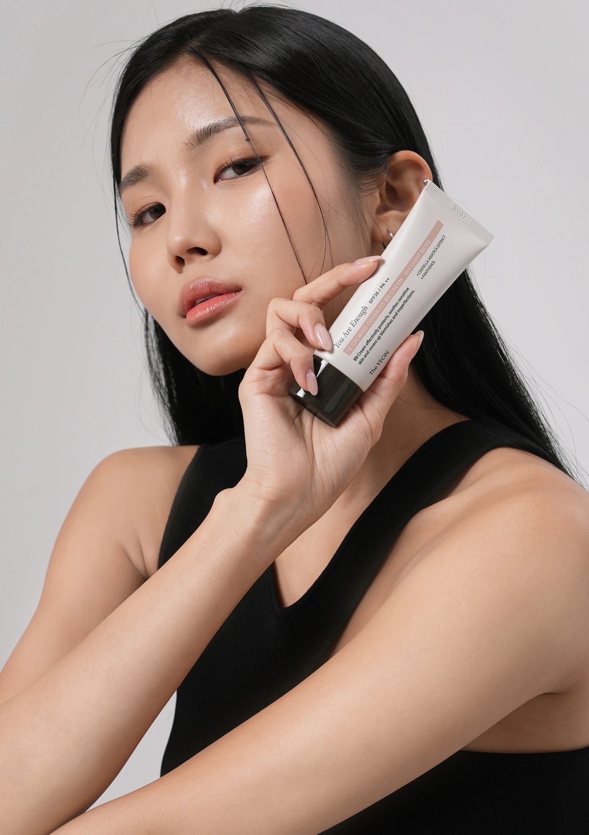 Woman holding a skincare product against a plain background